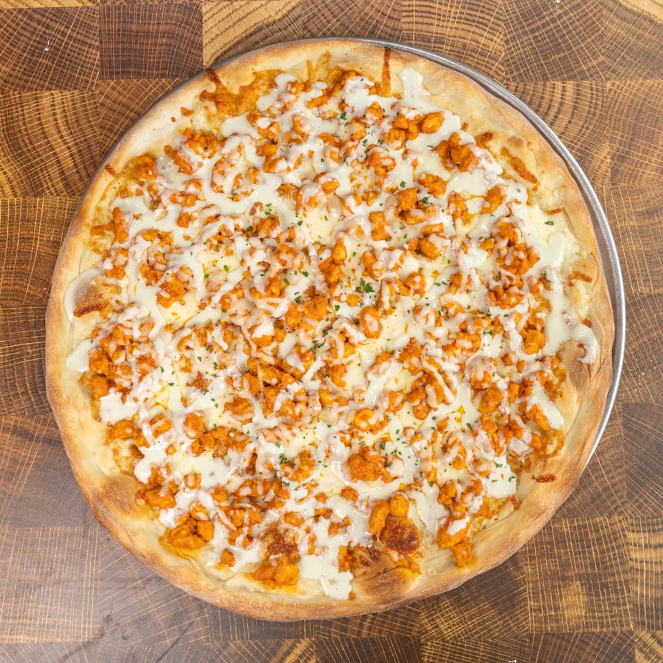Overhead view of a Buffalo chicken pizza with white sauce and parsley on a wooden table.