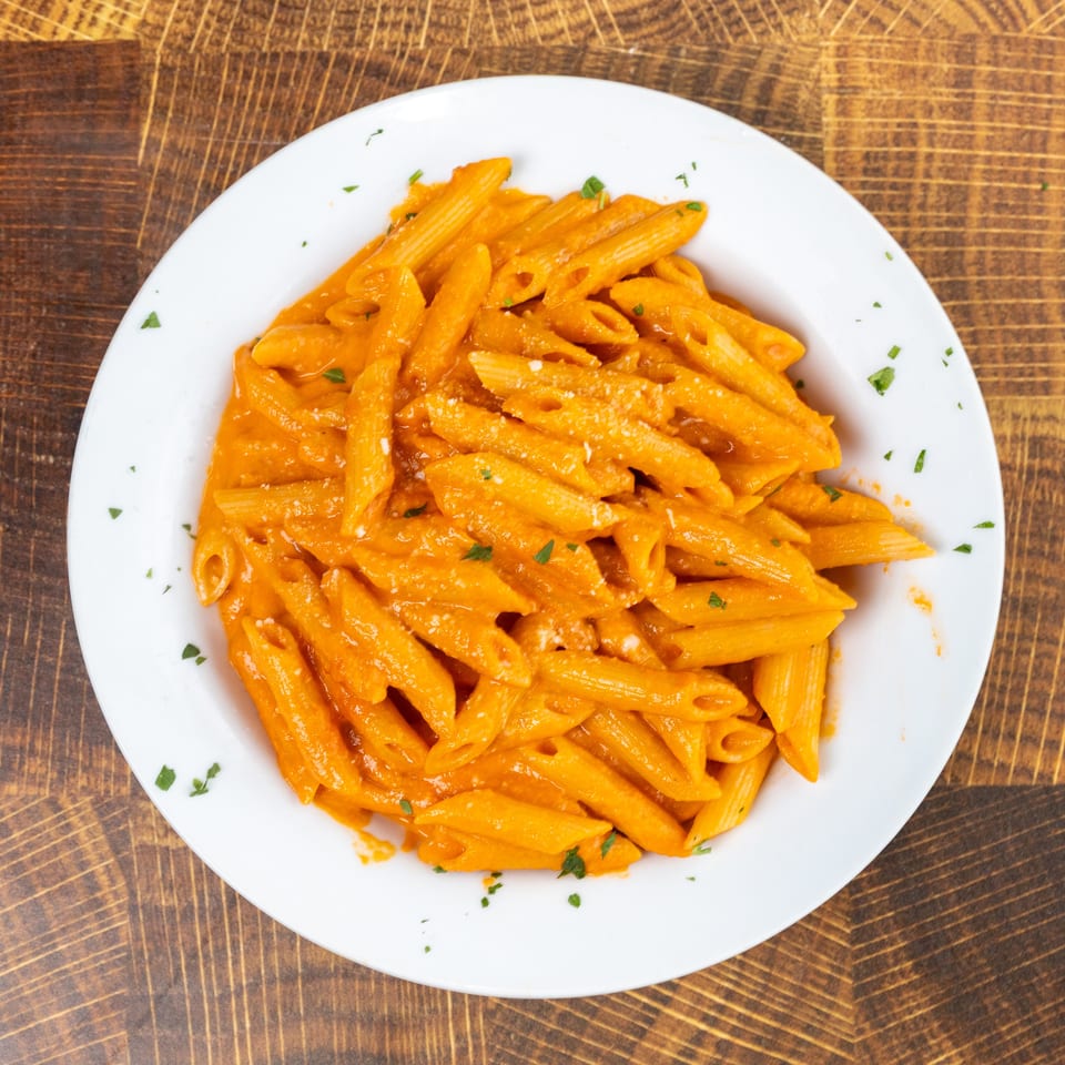 Penne pasta in a creamy orange sauce, garnished with parsley and parmesan cheese.