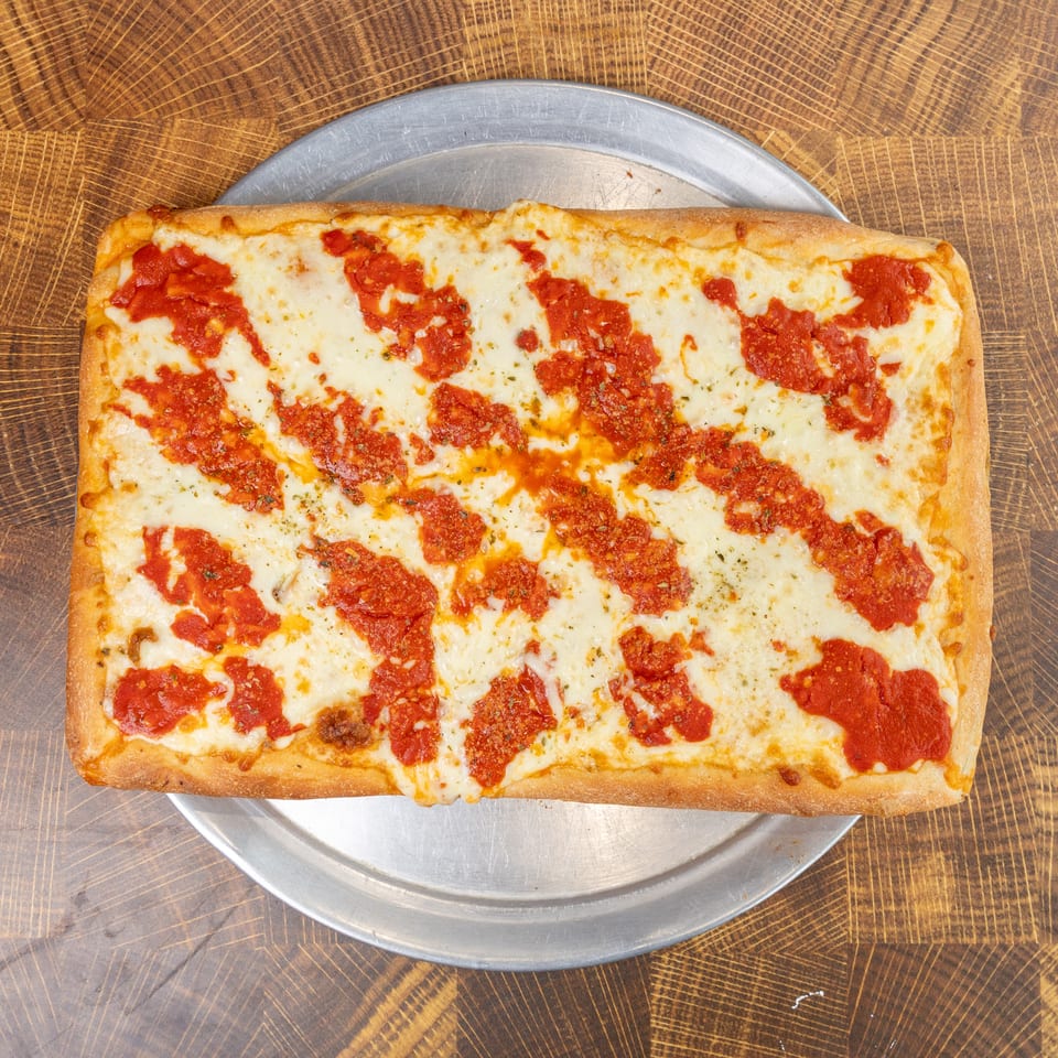 Rectangular Sicilian pizza with melted mozzarella cheese and red sauce stripes on a metal tray.