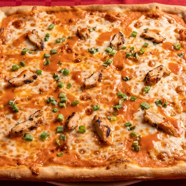 Square pizza with melted cheese, orange sauce, grilled chicken pieces, and chopped green onions.