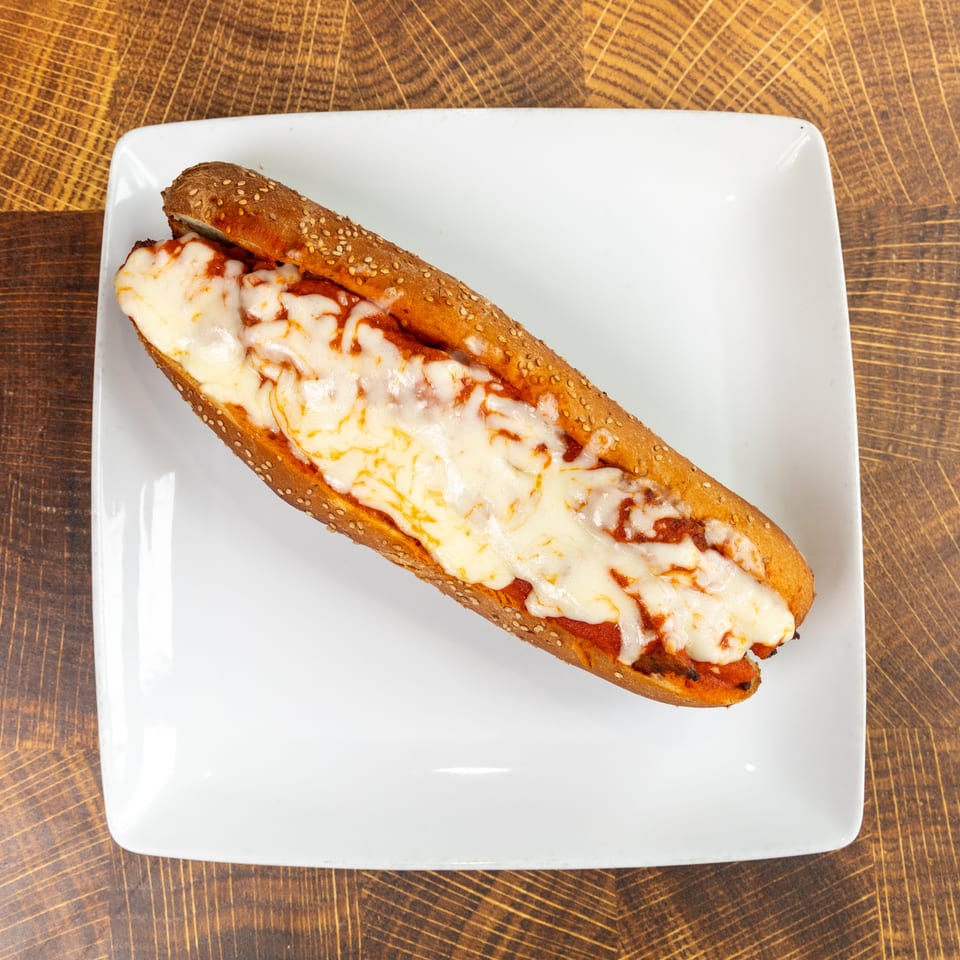 Meatball sub with melted mozzarella cheese and marinara sauce on a white plate.