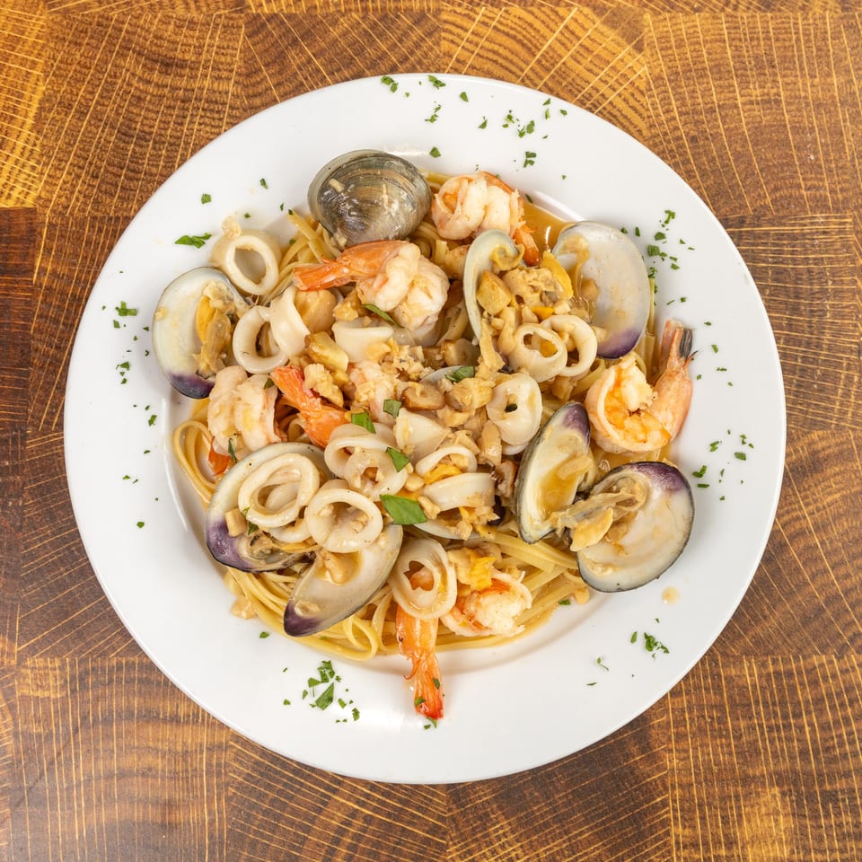 Seafood linguine with clams, shrimp, and calamari, garnished with parsley on a white plate.